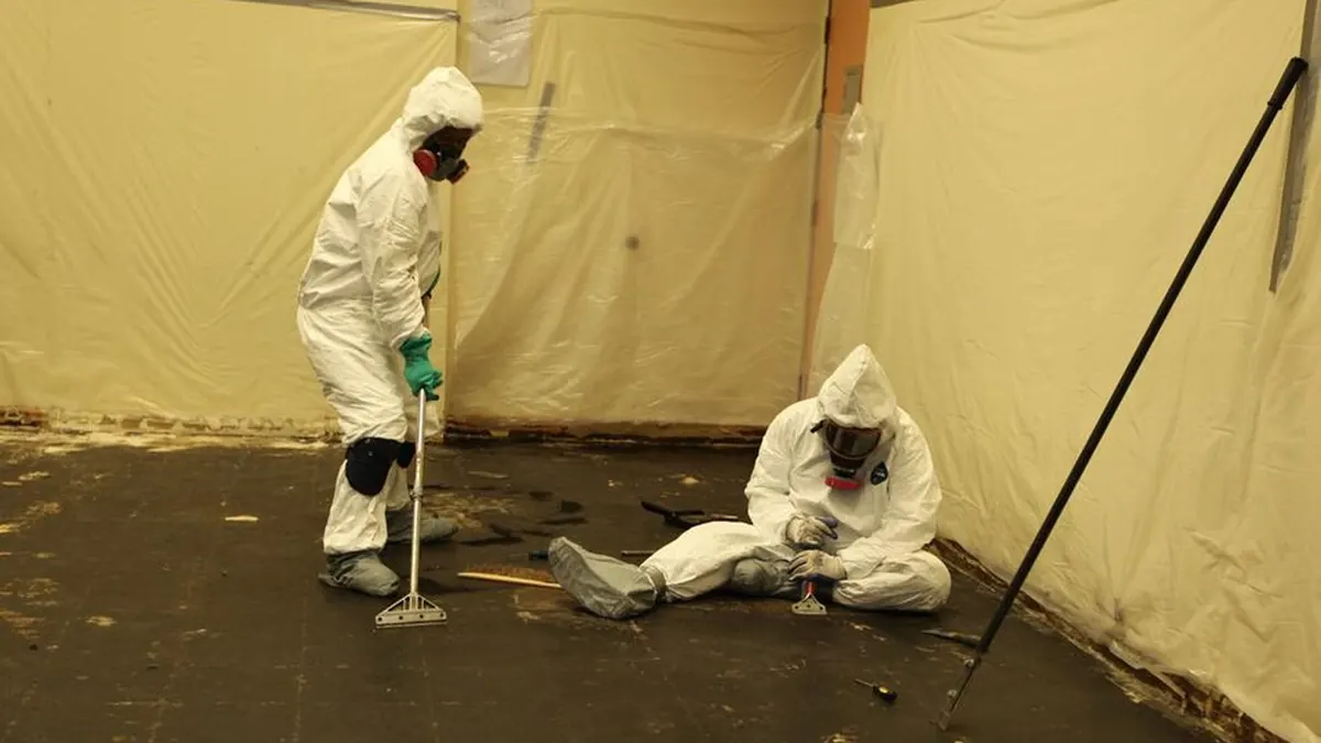 Asbestos abatement workers in protective suits inside a contained work area
